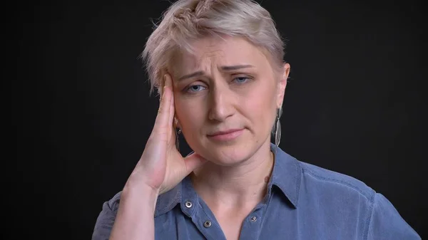 Nahaufnahme Porträt von erwachsenen attraktiven kaukasischen Frau mit Kopfschmerzen und Müdigkeit, während sie vor der Kamera mit Hintergrund isoliert auf schwarz — Stockfoto