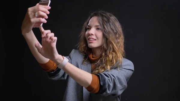 Closeup shoot of young attractive caucasian female taking selfies on the phone in front of the camera with background isolated on black — Stock Photo, Image