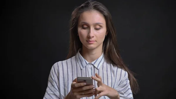 Closeup portrait of young beautiful brunette caucasian female texting on the phone in front of the camera with isolated background — Stock Photo, Image