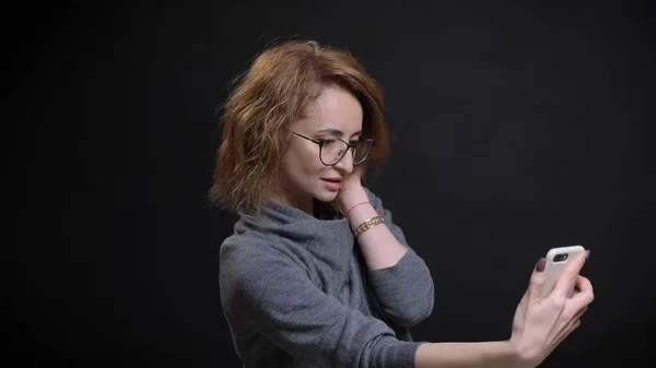 Closeup portrait of middle-aged extravagant red haired female in glasses taking selfies on the phone and posing in front of the camera — Stock Photo, Image