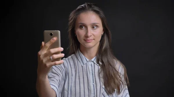 Closeup portrait of young pretty caucasian female taking selfies on the phone and posing in front of the camera with isolated background — Stock Photo, Image