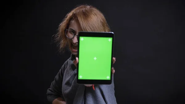 Nahaufnahme Porträt einer extravaganten rothaarigen Frau mittleren Alters mit Brille, die das Tablet benutzt und der Kamera lächelnd den grünen Bildschirm zeigt — Stockfoto