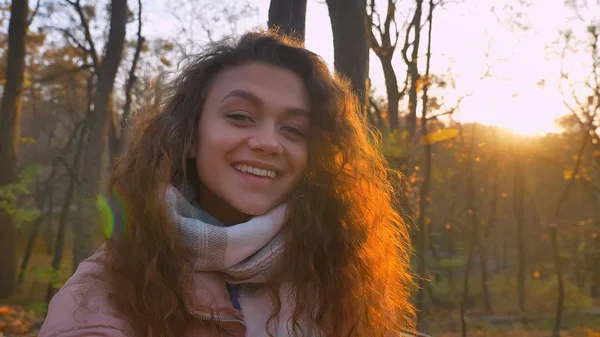 Selfie-foto av curly-haired kaukasiska flicka tittar leende in kameran i soliga höstlig park. — Stockfoto