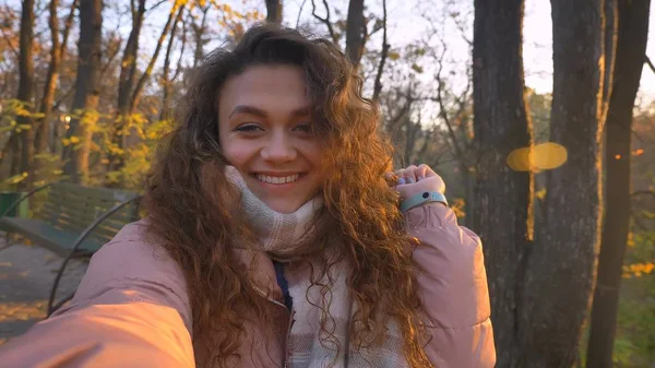 Selfie-foto van curly-haired Kaukasische meisje kijken vreugdevol in camera in zonnige herfst park. — Stockfoto