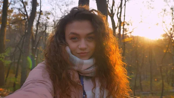 Selfie-foto av curly-haired kaukasiska flicka tittar leende in kameran och blinkningar vid det i soliga höstlig park. — Stockfoto