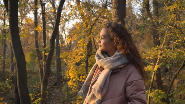 Portrait in profile of smiling curly-haired caucasian girl walking in autumnal park and observing the beauty.