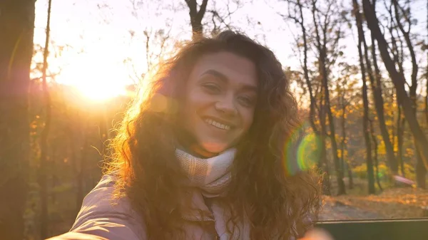 Selfie-foto de bonito de cabelos cacheados caucasiano menina assistindo alegremente em câmera no ensolarado parque outonal . — Fotografia de Stock