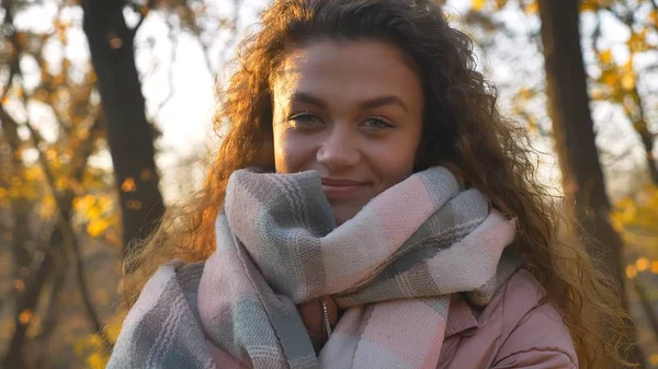 Porträtt av leende curly-haired kaukasiska flicka titta in kameran i höstlig park. — Stockfoto