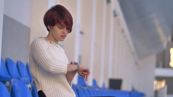 Retrato de una joven caucásica concentrada de pelo rosa sentada en el estadio y mirando sus relojes . — Foto de Stock