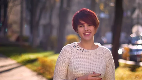 Retrato de una joven chica caucásica de pelo rosa mirando sonriente a la cámara sobre el soleado fondo del parque . — Foto de Stock