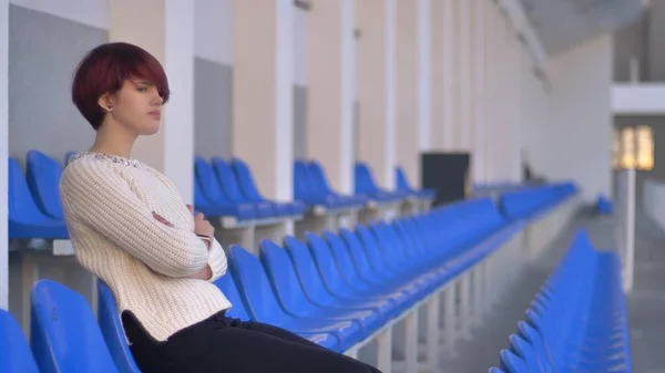 Retrato de una triste joven caucásica de pelo rosa sentada en el estadio con los brazos cruzados y pensando . — Foto de Stock