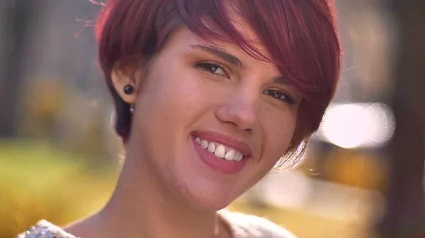 Close-up portret młodego fajny kaukaski haired Dziewczyna oglądania z flirty uśmiech do kamery na tle słoneczny park. — Zdjęcie stockowe