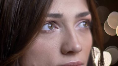 Yakın çekim göz-portresi güzel beyaz esmer kız yukarı doğru olarak izlerken ışıkları arka plan bulanık.