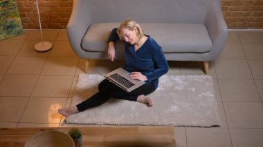 Katta oturan ve sevinçle rahat ev atmosferi içinde laptop içine izlerken beyaz kadın kıdemli portresi.