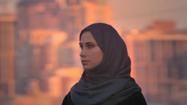 Nahaufnahme Seitenansicht Porträt einer jungen attraktiven Frau im Hijab, die direkt in die Kamera schaut, mit einer Stadt im Hintergrund. — Stockfoto