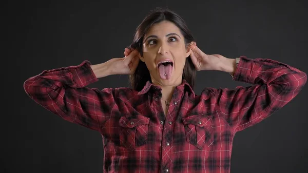 Retrato de la joven hermosa chica de pelo largo en camisa trenzada haciendo caras divertidas en la cámara sobre fondo negro . —  Fotos de Stock