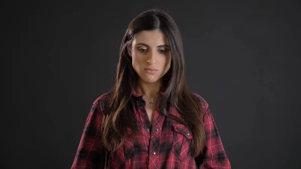 Retrato de la joven hermosa chica de pelo largo en camisa trenzada mirando tristemente hacia abajo sobre fondo negro . — Foto de Stock