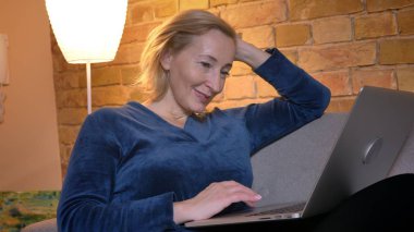 Kanepede oturan ve rahat ev atmosferi içinde memnuniyetle laptop ile çalışan üst düzey beyaz Bayan portresi.