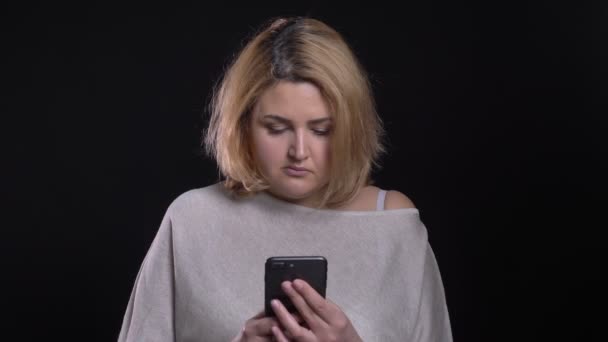 Geconcentreerde blonde korthaar overgewicht zakenvrouw horloges serieus in smartphone op zwarte achtergrond. — Stockvideo