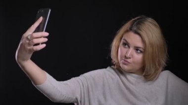 Güzel sarışın kısa saçlı kilolu işkadını flört selfie-fotoğrafları yapma siyah arka plan üzerine smartphone kullanarak.