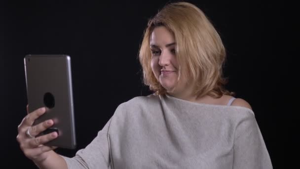 Schattige blonde korthaar overgewicht zakenvrouw praten vreugdevol in videochat op tablet op zwarte achtergrond. — Stockvideo