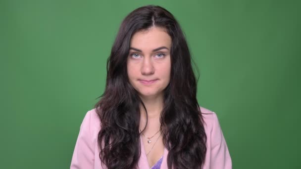 Portrait de jeune femme d'affaires brune en veste rose regardant timidement dans la caméra sur fond vert . — Video