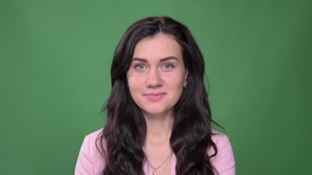 Retrato de joven mujer de negocios morena en chaqueta rosa sonriendo tímidamente en la cámara sobre fondo verde . — Vídeos de Stock