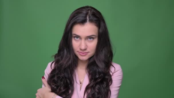 Retrato de una joven empresaria morena en chaqueta rosa posando sonriente pero tímidamente en la cámara sobre fondo verde . — Vídeo de stock