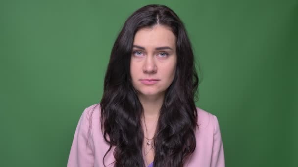 Portret van brunette zakenvrouw in roze jas horloges met veel pijn en verdriet in camera op groene achtergrond — Stockvideo