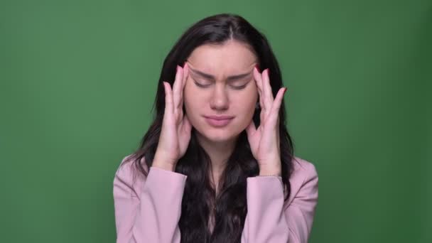 Porträtt av brunett affärskvinna i rosa jacka gör massage från huvudvärk på grön bakgrund. — Stockvideo