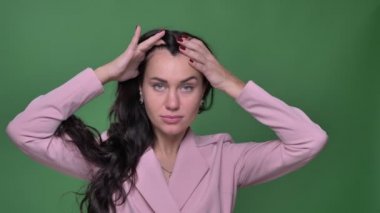 Güzel esmer iş kadını saçlarını düzeltmesine ve modaya uygun içine yeşil arka plan kameraya poz pembe ceket.