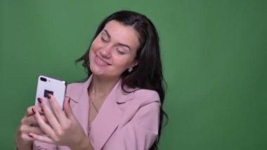 Selfie-fotoğrafları yapma ve onları smartphone yeşil zemin üzerine izlerken pembe ceket genç esmer vloger.