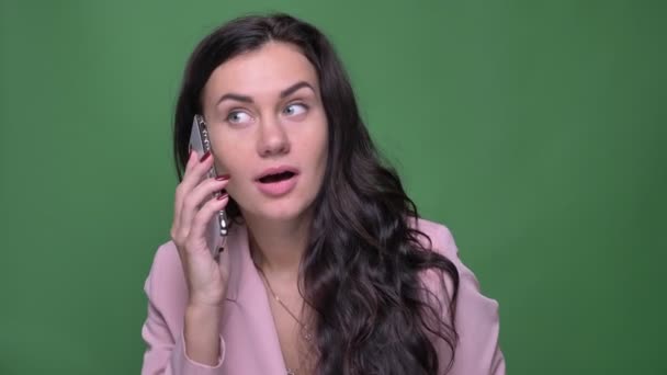 Retrato de una joven morena con chaqueta rosa hablando sonriente en un smartphone sobre fondo verde . — Vídeos de Stock