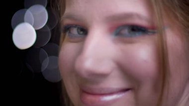 Yakın çekim portre profil kameraya dönüm ve kameraya gülümseyen sarışın model ışık arka plan bulanık.