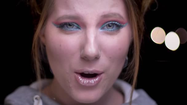 Close-up portret van blond meisje met kleurrijke make-up waarop groot geluk emotioneel wazig lights achtergrond. — Stockvideo