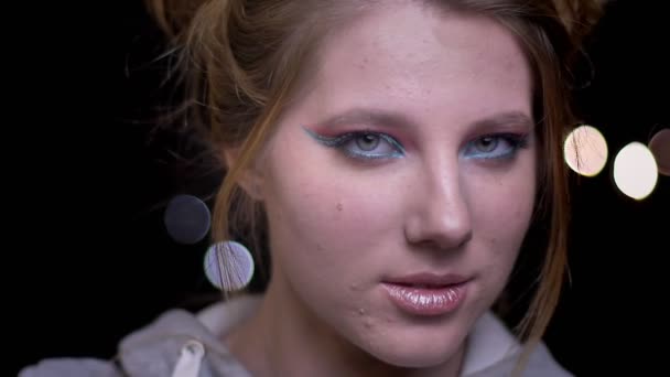 Atractiva modelo rubia con maquillaje brillante posando a la moda y tocando su cabello sobre un fondo de luces borrosas . — Vídeos de Stock