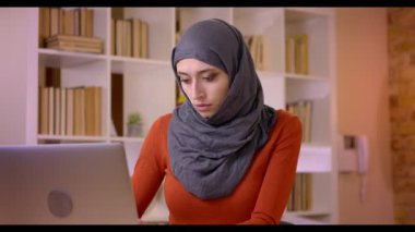 Closeup çekim dizüstü bilgisayarda yazarak ve mutlu bir şekilde kapalı ofiste gülümseyen genç çekici Müslüman kadın çalışanın