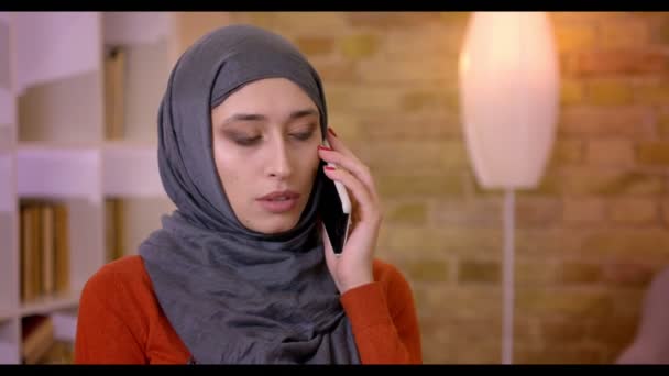 Closeup çekim genç çekici Müslüman kadın çalışanın hijab rahat duygusal kapalı ofis içinde belgili tanımlık laptop önünde oturan telefonda konuşuyor — Stok video