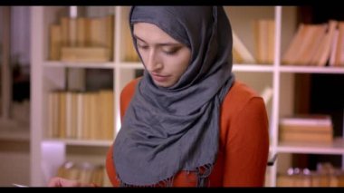Closeup çekim genç çekici Müslüman kadın öğrencinin Tesettür kapalı kütüphanede bir sınav ayakta hazırlama bir kitap okuma