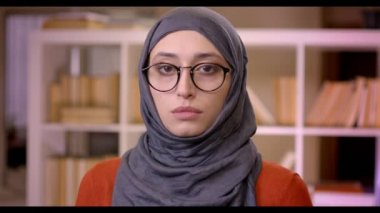 Closeup çekim genç çekici Müslüman kadın öğrencilerin Türban ve gözlük kamera ayakta kapalı kütüphanede bakarak