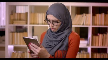 Closeup çekim genç çekici Müslüman kadın öğrencilerin tablet ayakta kapalı kütüphanede kullanarak Hicap