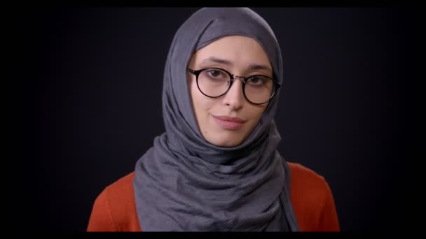 Nahaufnahme einer jungen attraktiven muslimischen Frau im Hijab, die in die Kamera blickt und vor schwarzem Hintergrund lächelt — Stockvideo