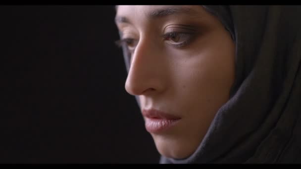 Primo piano vista laterale tiro di giovane attraente volto femminile musulmano in hijab guardando la fotocamera con sfondo isolato su nero — Video Stock