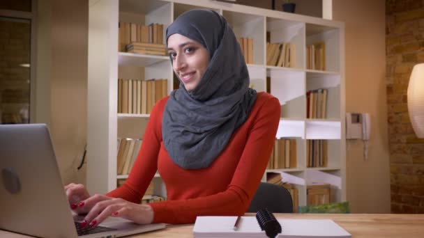 Vértes-lő a vonzó fiatal muzulmán üzletasszony, a hidzsáb sikeresen dolgozik a laptop, és mosolyogva, boldogan bent az irodában — Stock videók