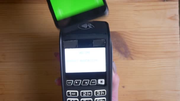 Tiro de perto de um terminal de pagamento que está sendo usado para pagamento por um anúncio no telefone com tela verde chroma-key dentro de casa. Caixa e cliente — Vídeo de Stock