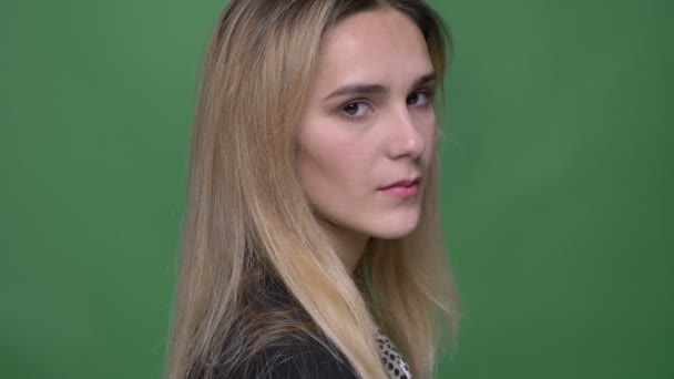 Крупный план молодой привлекательной хипстерской кавказской женщины, поворачивающейся и смотрящей прямо в камеру на фоне изолированного на зеленом фоне — стоковое видео