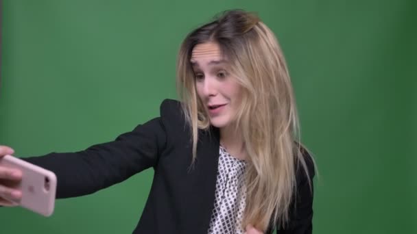 若い魅力的なヒップスターの白人女性のクローズアップシュートは、緑に孤立した背景を持つ電話でビデオ通話を持って — ストック動画