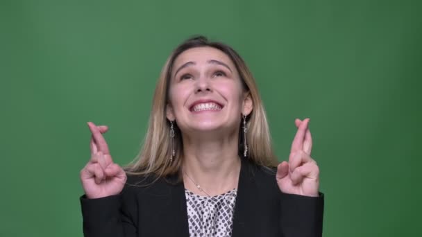 Closeup shoot of young attractive hipster caucasian female having her fingers crossed anxiously and praying with background isolated on green — Stock Video