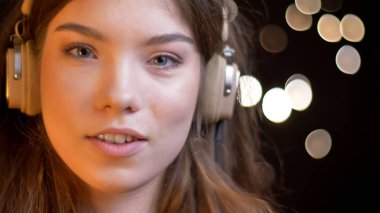 Closeup çekim genç sevimli beyaz kadın neşeyle bokeh arka ışıkları ile gülümseyen kamera düz seyir kulaklık