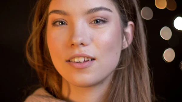 Närbild porträtt av ung kvinna i attraktiv kaukasiska leende och titta förföriskt på kameran med bokeh ljus på bakgrunden — Stockfoto